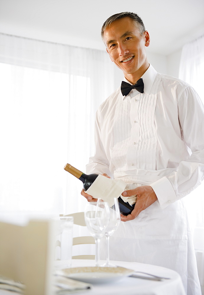 Smiling waiter holding champagne bottle and looking at camera