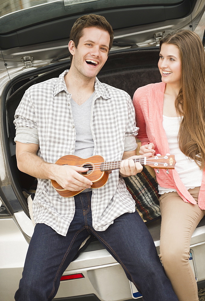 Happy young couple sitting in car boot with mandolin, USA, New Jersey, Jersey City