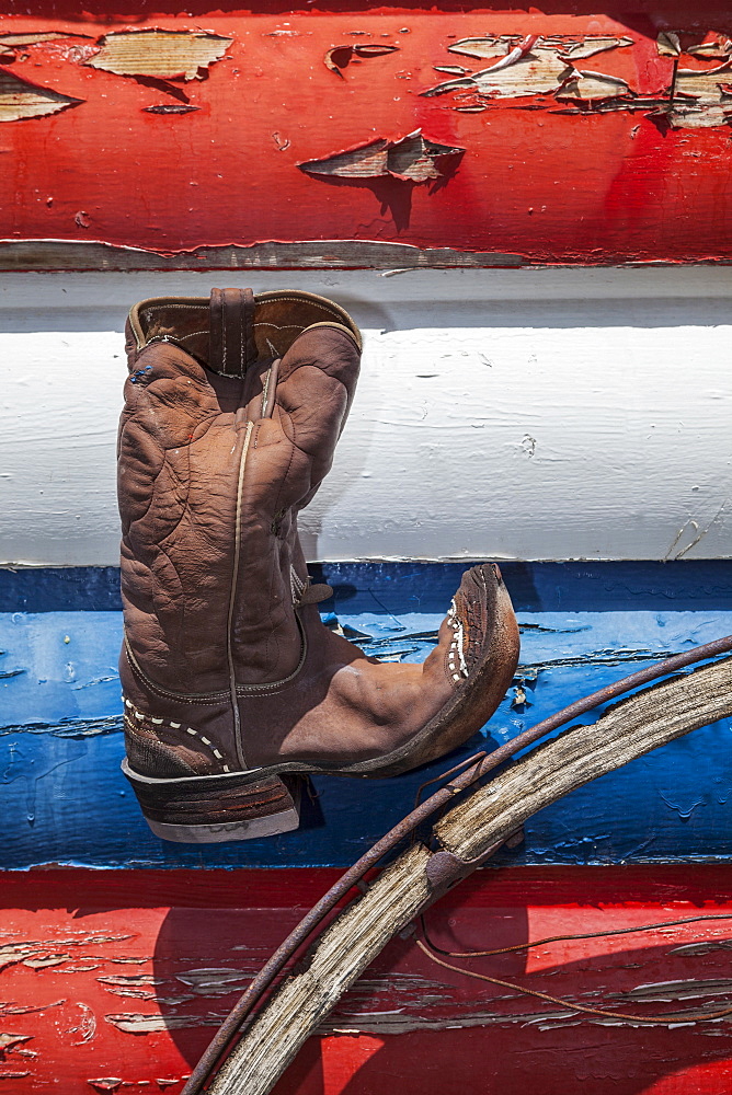 Cowboy boot and wagon wheel against red, white and blue peeling paint