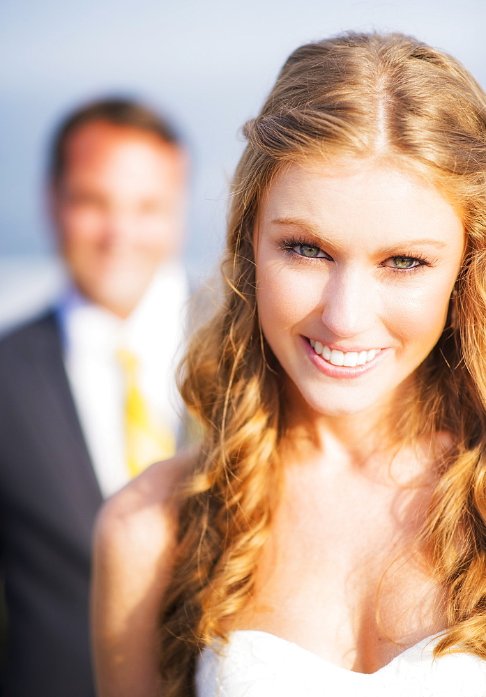 Portrait of smiling bride, groom in background