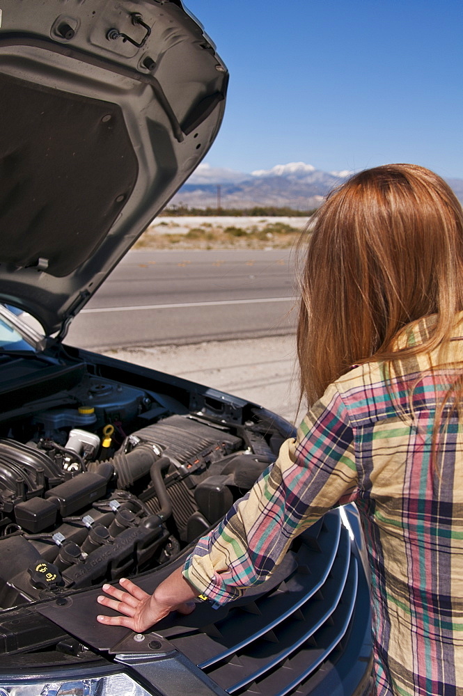 USA, California, Palm Springs, Woman standing in front of broken car in desert