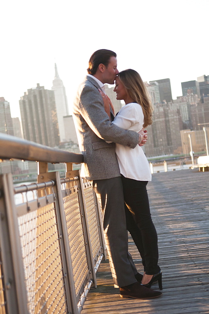 USA, New York, Long Island City, Young couple kissing on boardwalk, Manhattan skyline in background