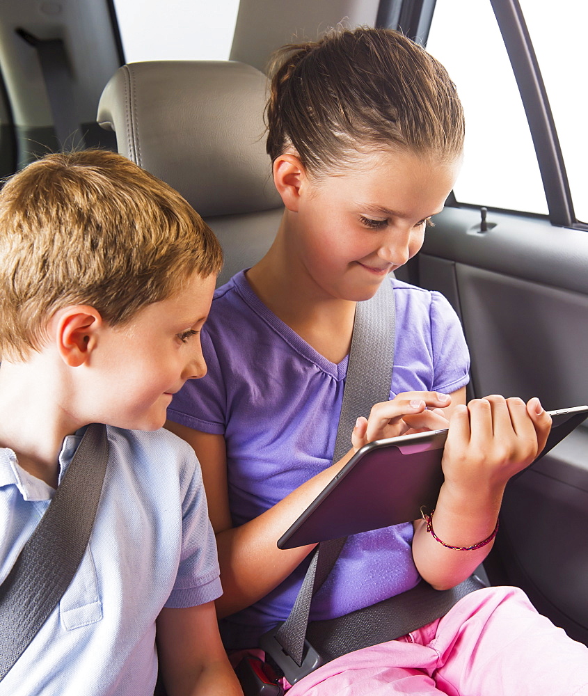 Boy (6-7) and girl (8-9) using digital tablet while sitting in car