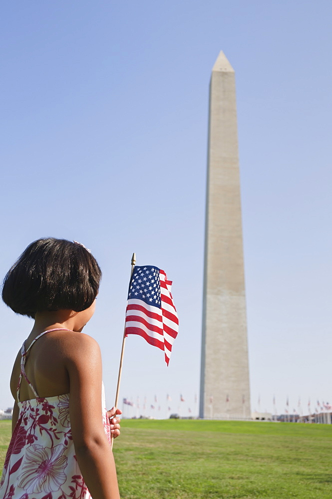 USA, Washington DC, girl (10-11) with US flag in front of Washington Monument