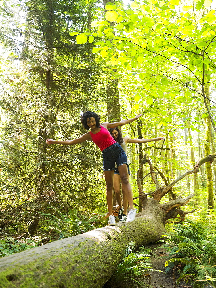 Two young women walking on log in forest, USA, Oregon, Portland