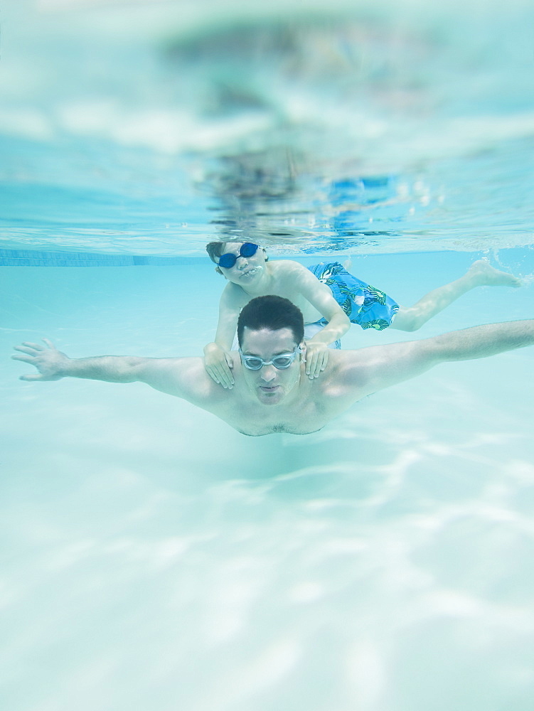 Boy swimming on father’s back underwater