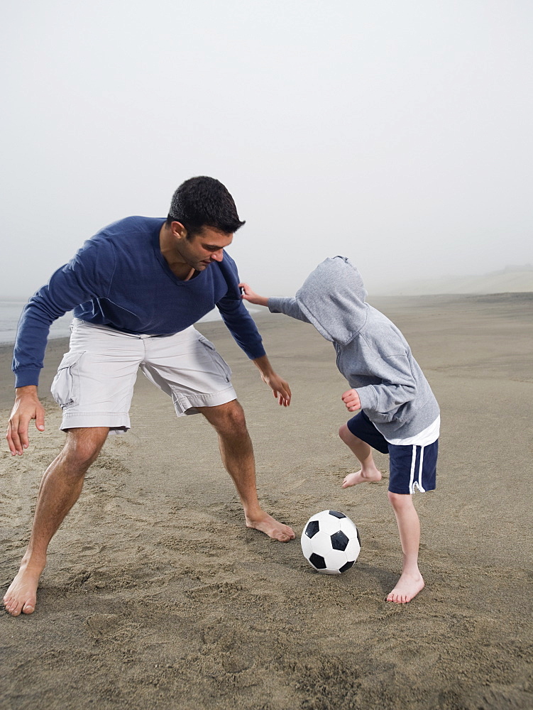 Father and son playing soccer on beach