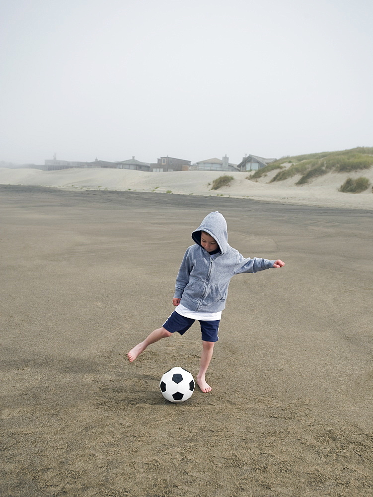 Boy kicking soccer ball on beach