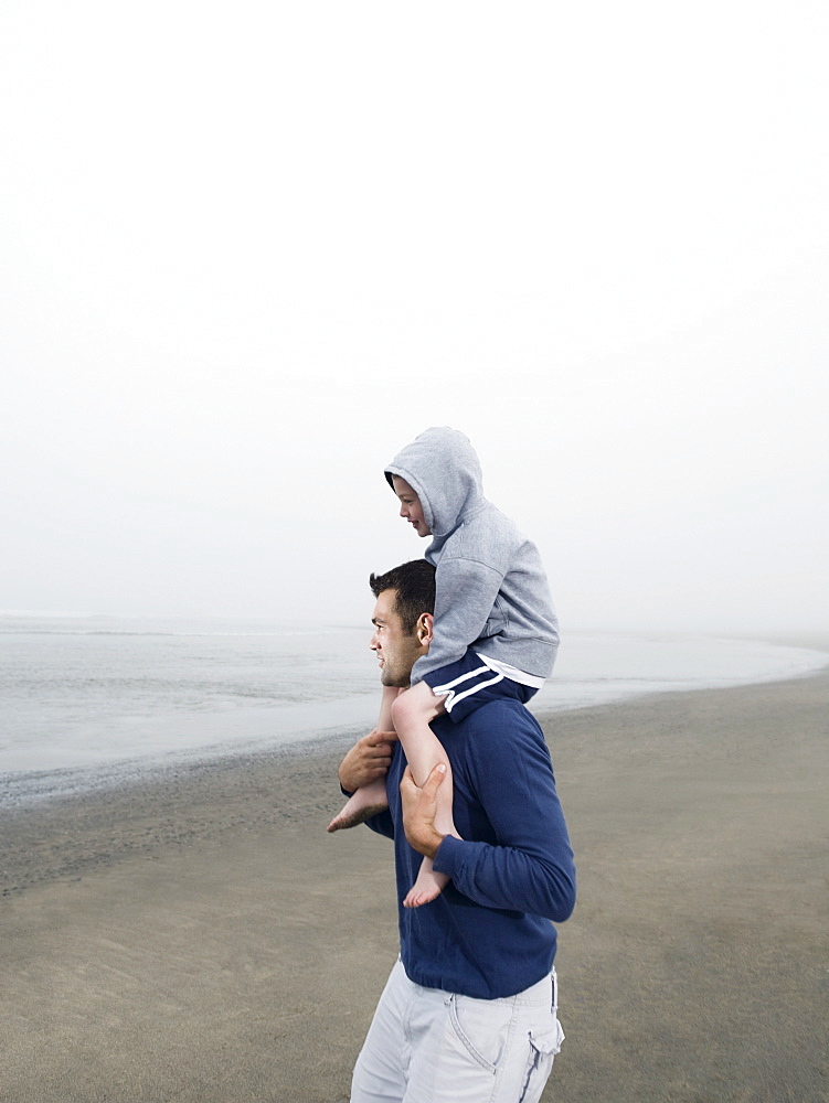 Father carrying son on shoulders on beach