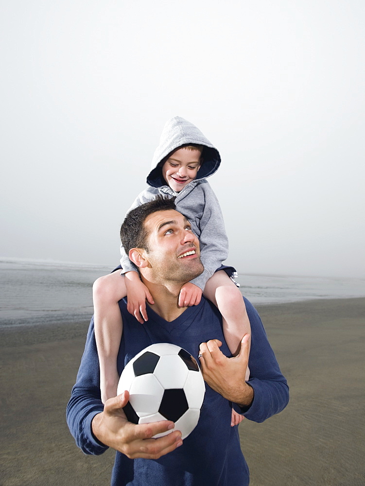 Father carrying son on shoulders and holding soccer ball on beach