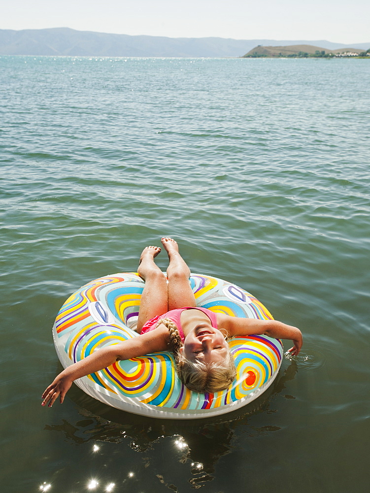 Girl (4-5) floating on water on inflatable ring and laughing