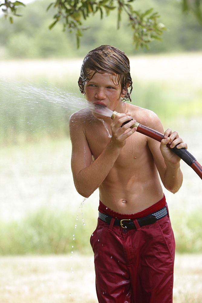 Boy (10-11) drinking from water hose in summer, Old Wick, New Jersey