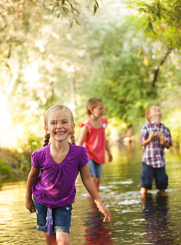 Little girl (4-5) in foreground standing in small stream with friends (6-7), Lehi, Utah