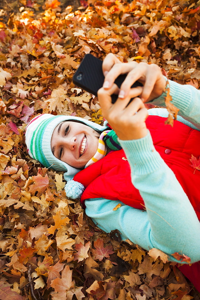 Young woman lying on autumn leaves and using 