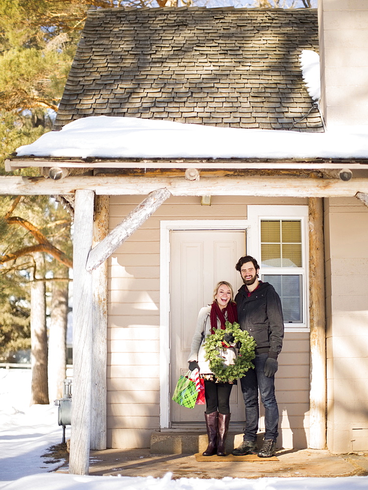 Young couple holding wreath standing in front of house, Salt Lake City, Utah