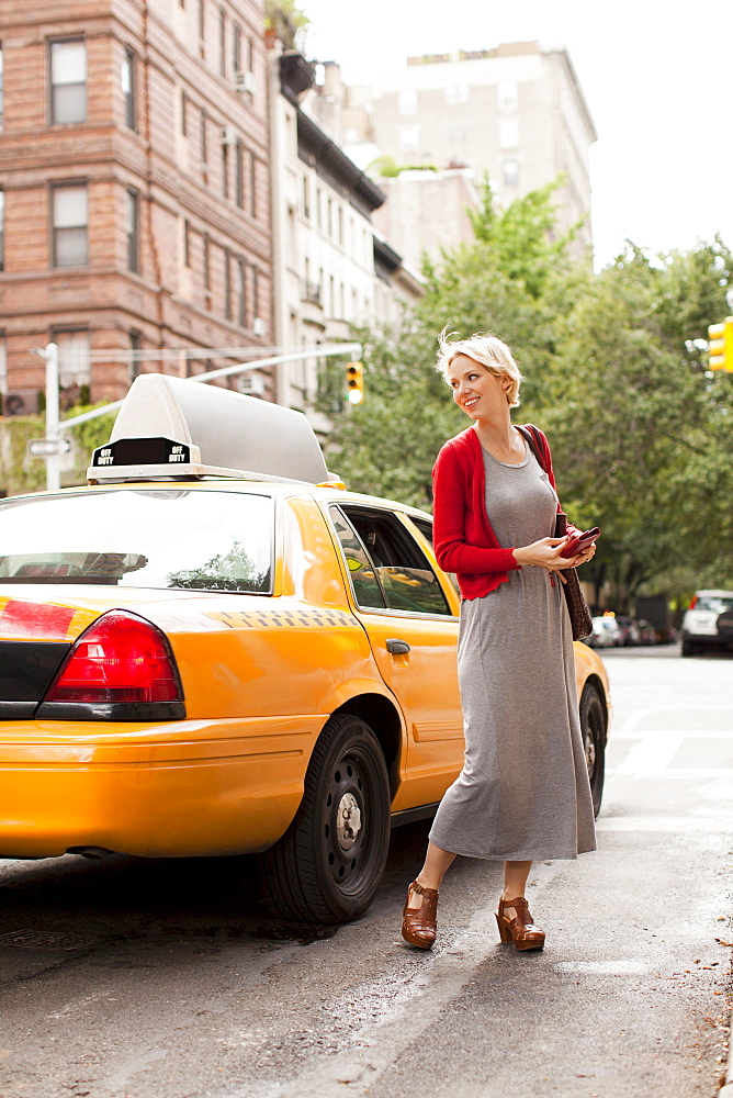 Woman standing next to yellow taxi on street, USA, New York State, New York