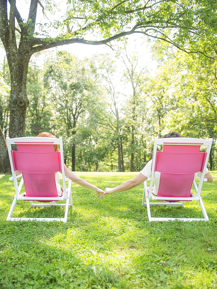 Couple sitting on deck chairs and holding hands, USA, New Jersey, Mendham