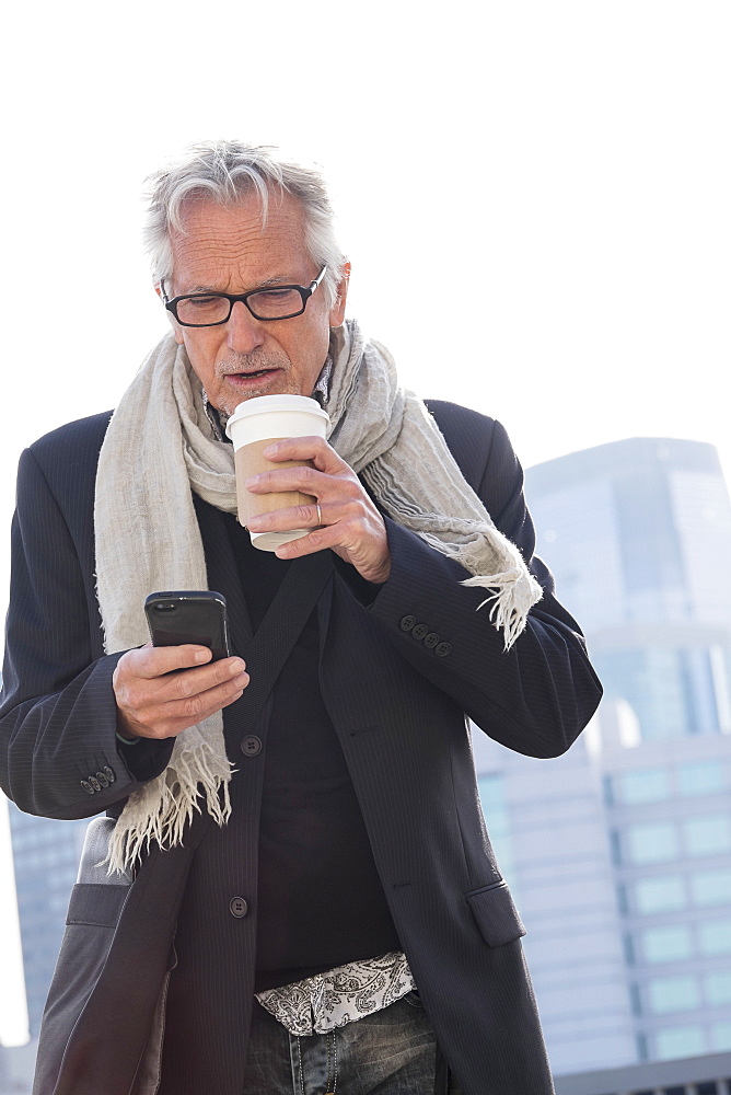 Man in street drinking coffee using smartphone