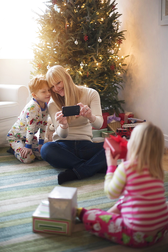 Mother with children (4-5, 6-7) opening christmas presents and taking photos