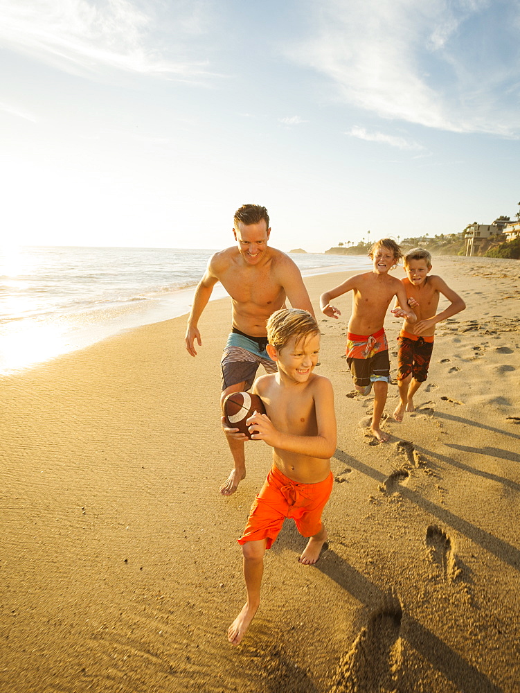 Father playing football on beach with his three sons (6-7, 10-11, 14-15), Laguna Beach, California