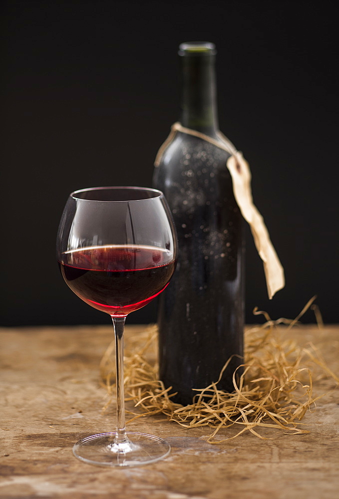 Still life with red wine glass and bottle on wooden table, studio shot