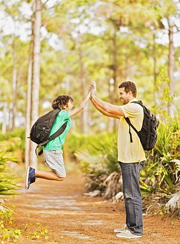 Father and son (12-13) doing high five in forest, Jupiter, Florida