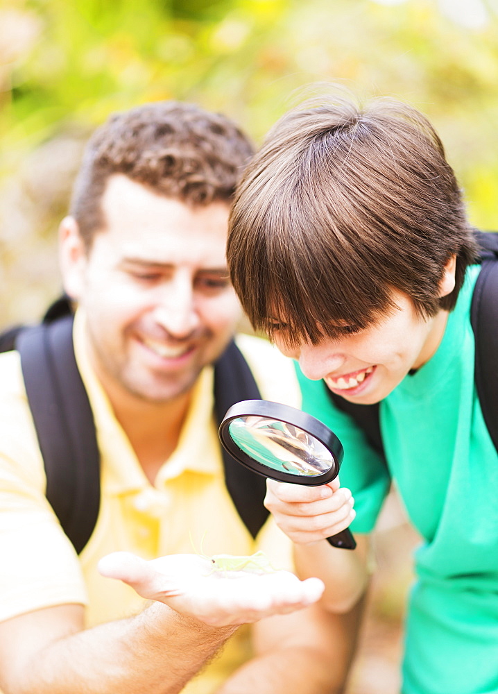 Father and son (12-13) watching butterfly with magnifying glass, Jupiter, Florida