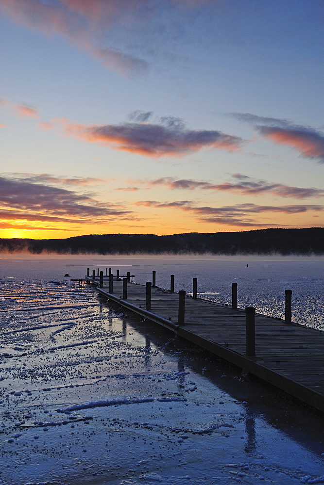 Jetty on frozen lake, hills in background at sunrise, Lake George, New York