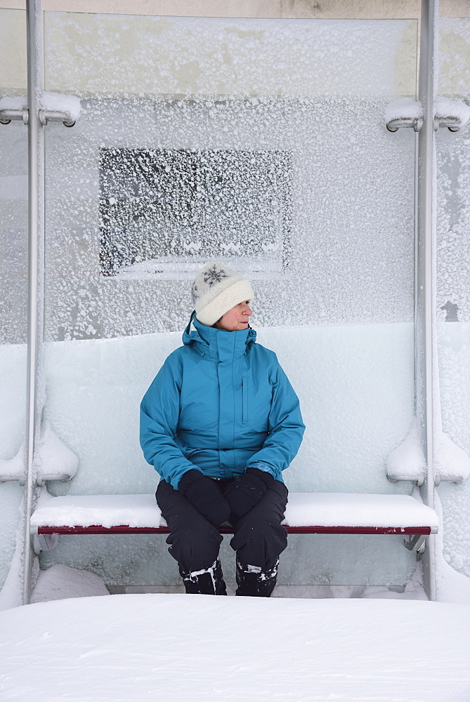 Middle aged woman sitting in bus stop, winter snow, Boston, Massachusetts 