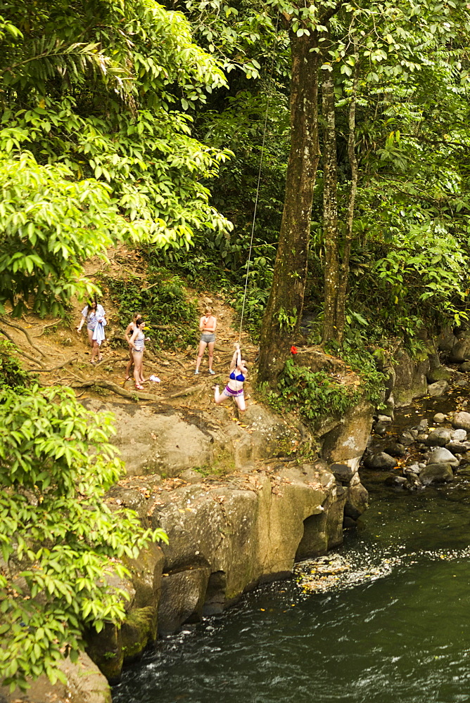 Women swinging on rope swing above river in distance, Costa Rica