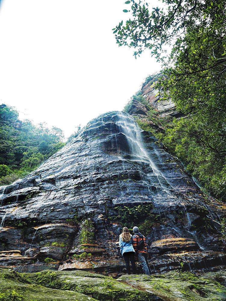 Australia, New South Wales, Blue Mountains National Park, Leura Cascades, Mid-adult couple at foot of rock with waterfall in forest