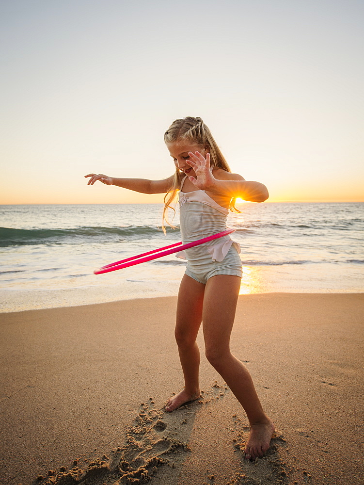 Girl (8-9) spinning plastic hoop on beach