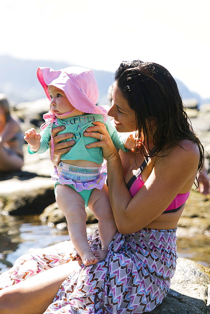 Woman holding baby daughter on rocks at beach