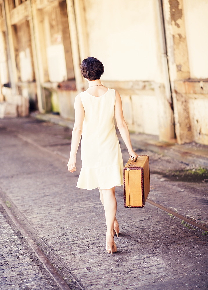 Rear view of woman in dress carrying suitcase at train station, USA, New Jersey, Jersey City 