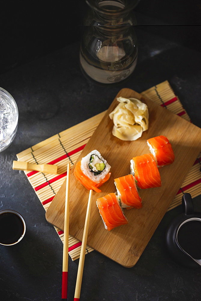 Salmon sushi on cutting board with pickled ginger and chopsticks