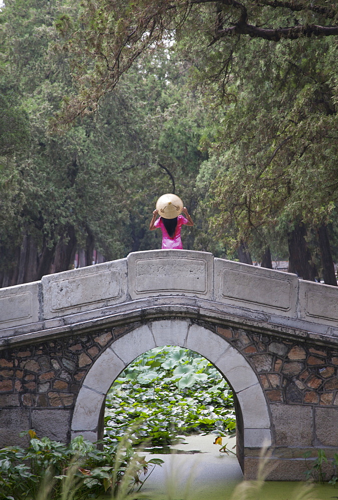 Woman wearing conical hat on arch bridge in Summer Palace gardens, Beijing, China