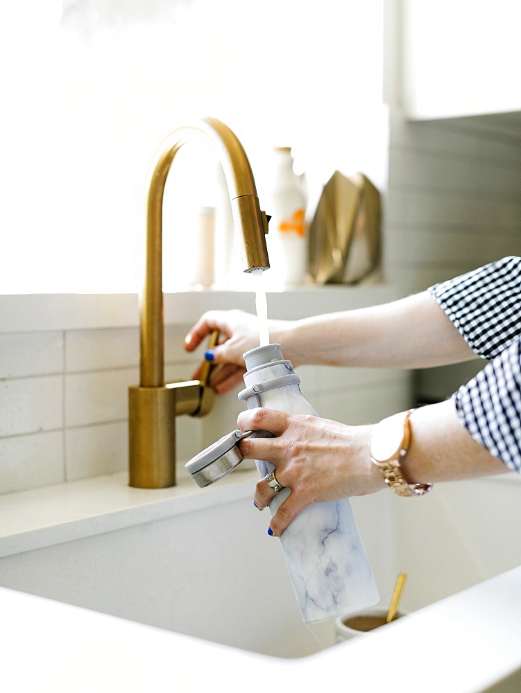 Hands of woman filling water bottle in kitchen sink