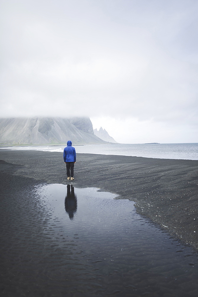 Man wearing blue coat on black sand beach in Kirkjubµjarklaustur, Iceland