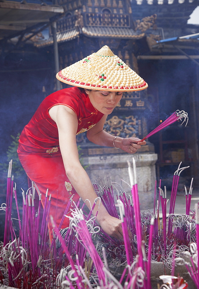 Woman lighting incense in temple in Lijang, Shangri-La Region, Yunnan Province, China