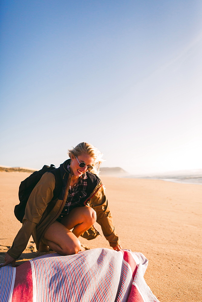 Smiling woman laying down towel on beach