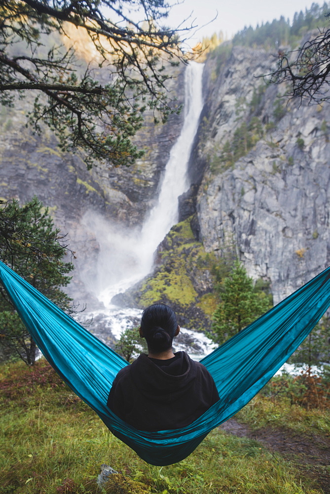 Young man resting in hammock by waterfall