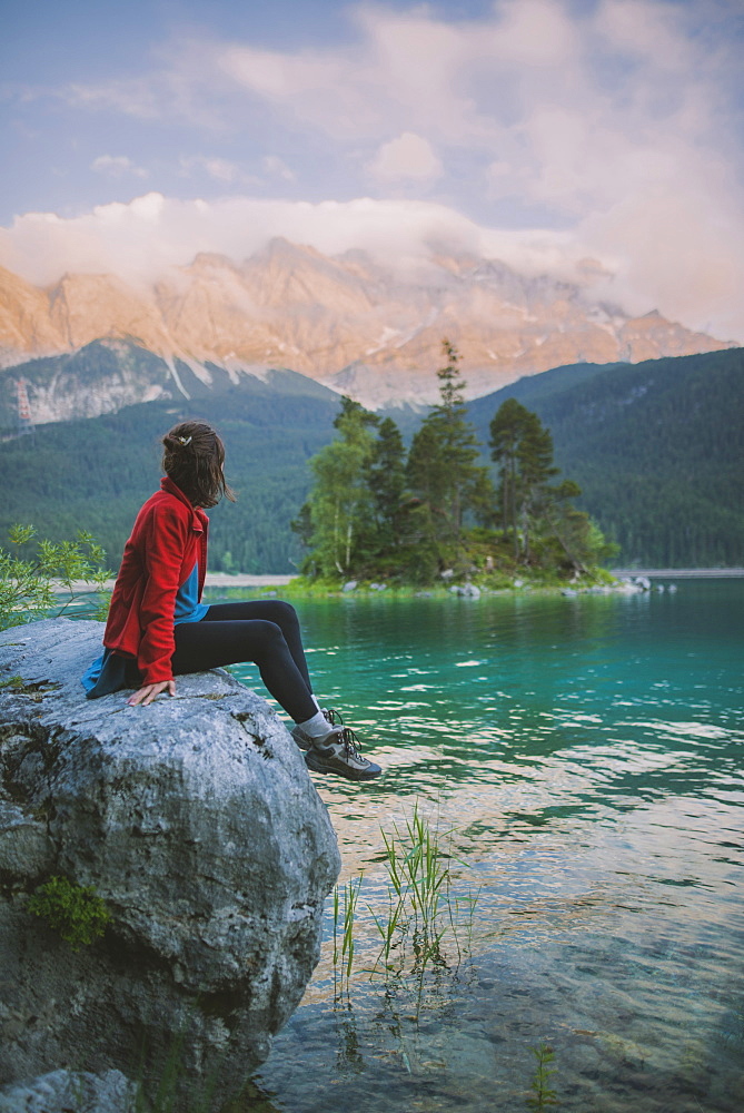 Germany, Bavaria, Eibsee, Young woman sitting on rock and looking at scenic view by Eibsee lake in Bavarian Alps