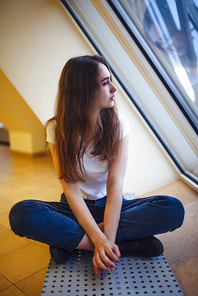 Young woman sitting on floor and looking through window