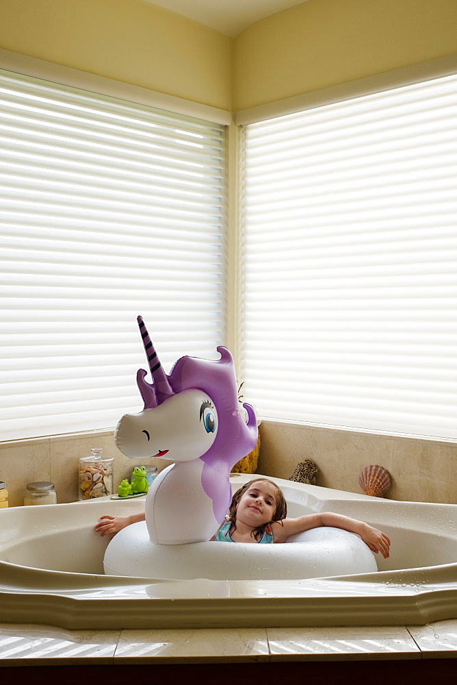 Girl (6-7) in unicorn shaped pool float in bathtub