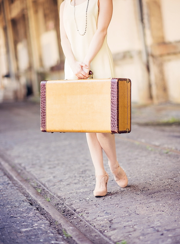 Low section of woman in dress holding suitcase at train station, USA, New Jersey, Jersey City 