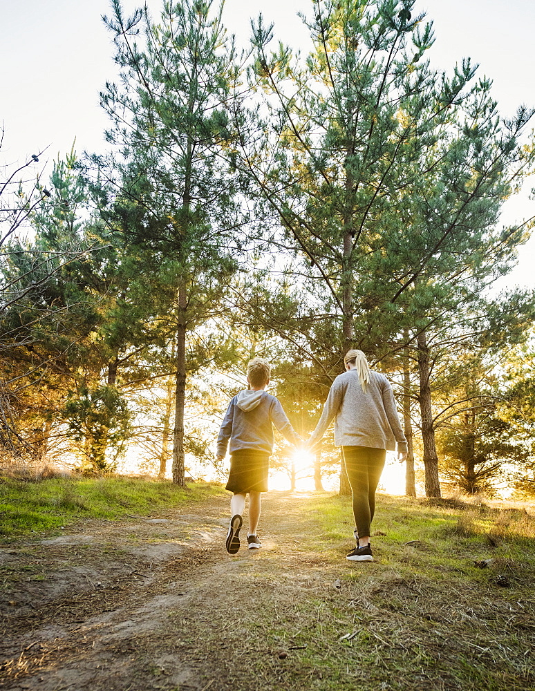 United States, California, Cambria, Rear view of boy (10-11) and girl (12-13) holding hands and walking in landscape at sunset