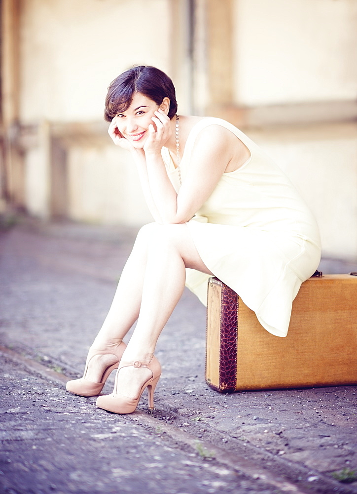 Woman in dress sitting on suitcase at train station, USA, New Jersey, Jersey City 