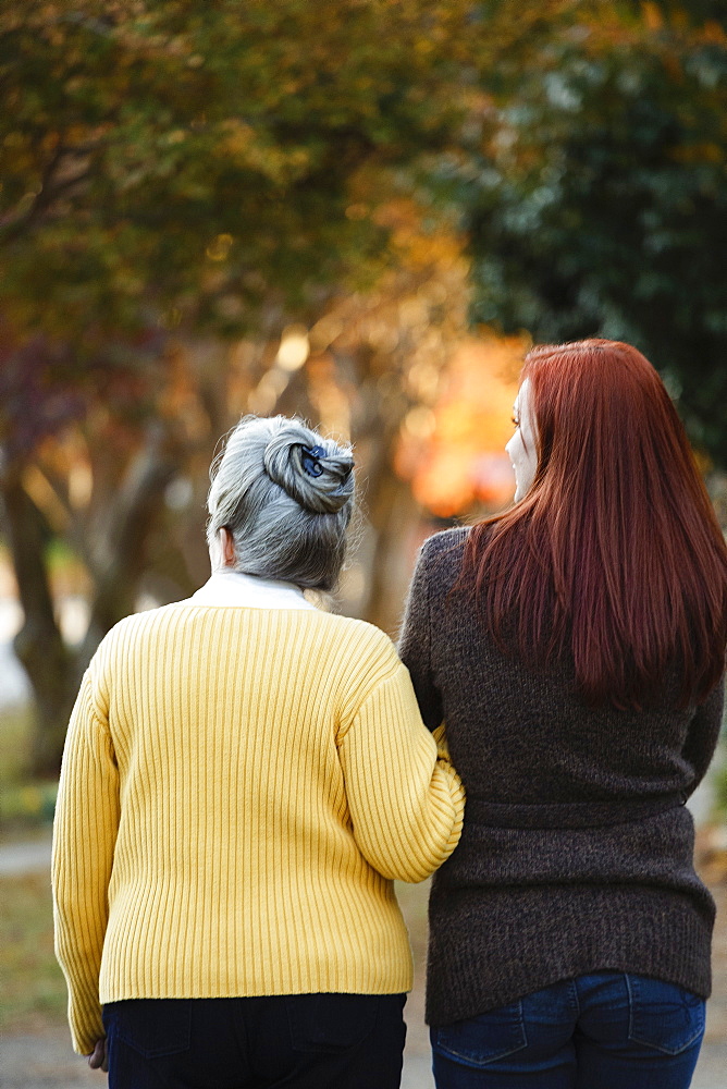 Rear view of senior woman and adult daughter strolling in autumn park