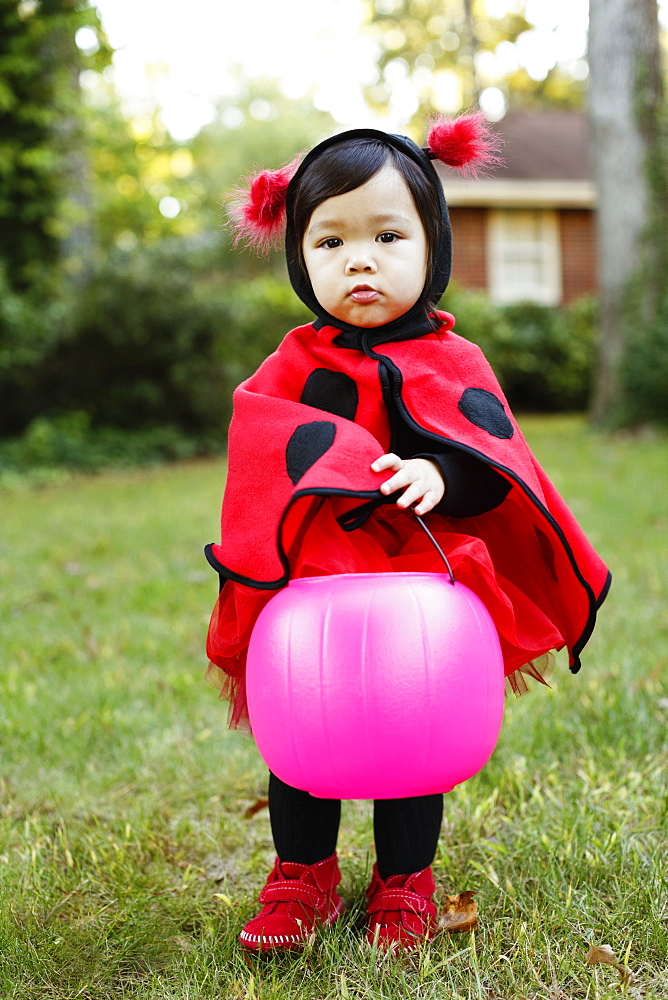 Young girl dressed up as ladybird with trick or treat bucket