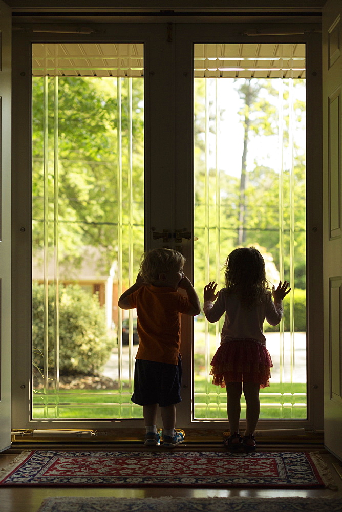 Male and female toddler friends silhouetted by patio door